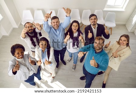 Team of satisfied people who make happy gesture by raising their hands with thumbs up demonstrating success. Top view of multiracial people expressing their support while standing in waiting room. Royalty-Free Stock Photo #2192421153