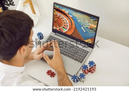 Young man playing poker on an online casino club website. Young guy sitting at a desk with poker chips and looking at the screen of his modern laptop computer. Online gambling and betting concept Royalty-Free Stock Photo #2192421193