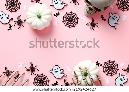 Happy Halloween pink background with cute decorations. Flat lay white pumpkins, ghosts, webs, skull, spiders. Halloween greeting card template.