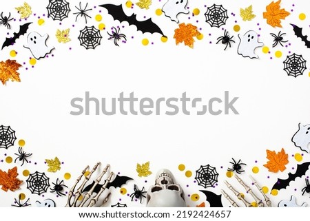 Happy Halloween holiday background. Flat lay composition with Halloween decorations, bats, ghosts, spiders, skull, skeleton arms on white table. Top view, copy space