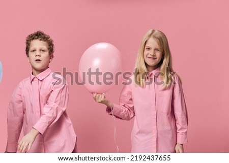 happy children boy and girl of school age smile cheerfully while standing on a pink background, the girl holds a pink balloon in her hand. Childhood, friendship, relationships