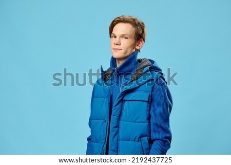 a handsome attractive young man in a warm blue jacket stands on a light blue background looking at the camera. Horizontal photo with empty space to insert advertising text