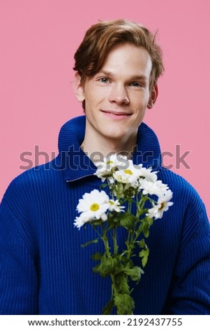 a handsome, good man stands with a bouquet of large daisies on a pink background