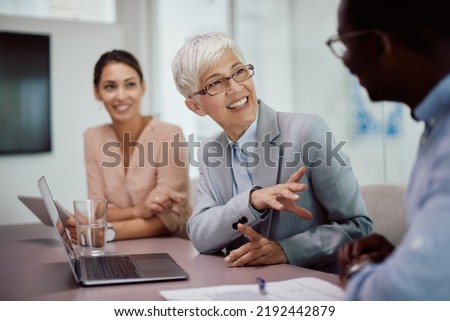Happy senior businesswoman communicating with colleagues while using laptop during the meeting in the office. Royalty-Free Stock Photo #2192442879