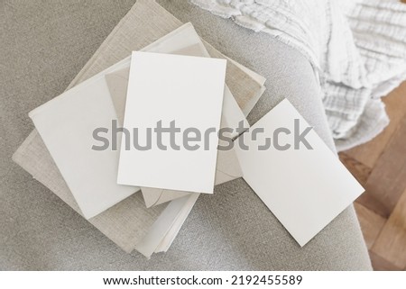 Set of blank greeting cards, invitations and craft envelopes mockups. Old books on linen sofa with cotton throw.Blurred wooden floor background. Home office, elegant stationery. Artistic display. 