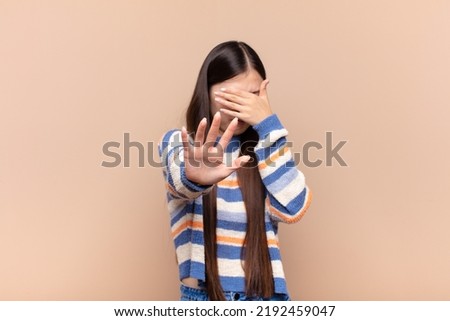 asian young woman covering face with hand and putting other hand up front to stop camera, refusing photos or pictures