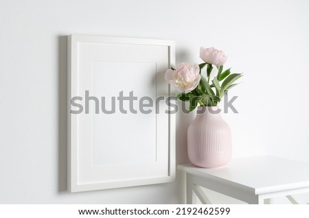 Frame mockup on white wall with peony flowers in vase, blank mockup for print or photo presentation