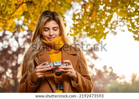 Young pretty girl analog photography enthusiast, taking pictures in the park in autumn  