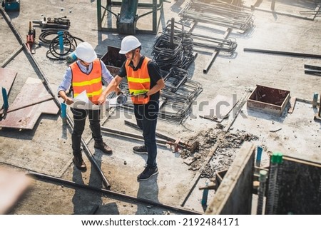 Two engineer in hardhat and orange jacket posing on building site. civil engineer or architect with hardhat on construction site checking schedule on plan. Two business man construction site engineer. Royalty-Free Stock Photo #2192484171