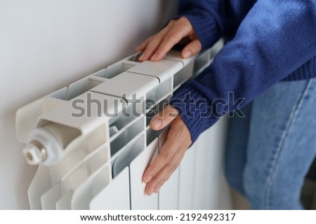 Closeup of woman warming her hands on the heater at home during cold winter days, top view. Female getting warm up her arms over radiator. Concept of heating season, cold weather.  Royalty-Free Stock Photo #2192492317