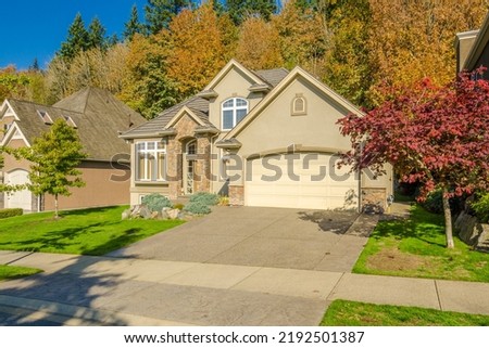 two story stucco luxury house with garage door, big tree and nice Fall Foliage landscape in Vancouver, Canada Royalty-Free Stock Photo #2192501387