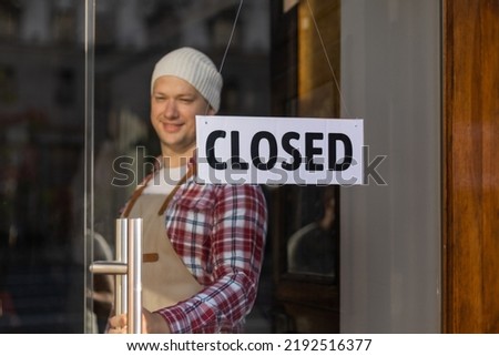 Handsome bar owner standing near sign board CLOSED, which hanging on door of cafe