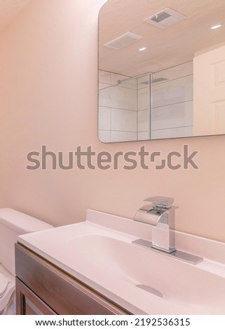 Vertical Corner of a bathroom with toilet and wooden flooring. There is a shower stall with aluminum door handle and ceramic tile walls and vanity sink with round cut mirror on the wall.