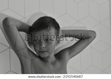 A black and white photo of a boy standing leaning against a wall with his elbows up.