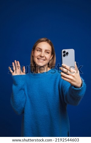Young beautiful girl taking selfie or making videocall waving to camera over isolated blue background