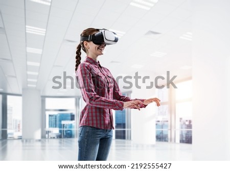 Young woman wearing virtual reality helmet in modern office interior. Mixed media