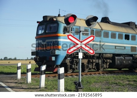 Forbidding red traffic light and roadsign on one way railway crossing on old diesel locomotive train background on suburban road at summer day