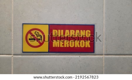 "Dilarang merokok" means No smoking. No smoking sign on the wall