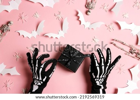 Female hands in funny spooky glove with a gift and Halloween decorations on pastel pink background. Flat lay, top view.
