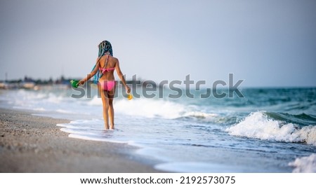 Funny slender cheerful girl playing with small waves, kicking their feet and spinning in place under the warm bright summer sun enjoying the long-awaited vacation
