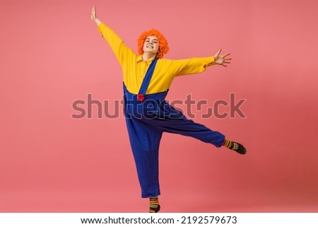 a cheerful clown in a wig and a yellow-blue suit dances on one leg on a colored background