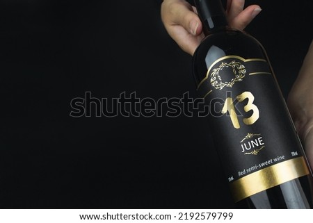 June 13rd. Day 13 of month, Calendar date. Hands hold bottle of red wine with a calendar date on label.  Summer month, day of the year concept