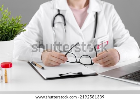 The doctor holds glasses in his hands while sitting at a white table.