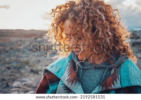 Side portrait of attractive woman with blonde coloured long curly hair looking down and enjoying outdoors nature feeling. Travel adult female people concept lifestyle with desert in background Royalty-Free Stock Photo #2192581531