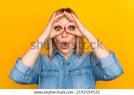 Happy cute surprised girl looking at camera through fingers over bright color background.