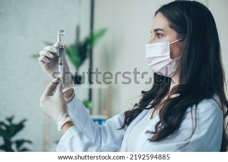 Doctor with medical mask and gloves preparing a vaccine in syringe for injecting the patient at hospital. Doctor or nurse with syringe preparing for injection