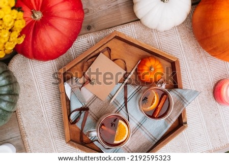 Top view cups with hot spiced tea with star anise, cinnamon stick, slice of orange on the wooden tray with decorative pumpkin, flowers and blank postcard. Cozy autumn. Tea time ideas. Selective