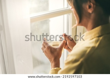 Young woman drinking a cup of tea looking outside the window Portrait of a girl enjoying free time at home. Middle aged female with a drink in the hand look through the door. Lifestyle leisure concept Royalty-Free Stock Photo #2192597103