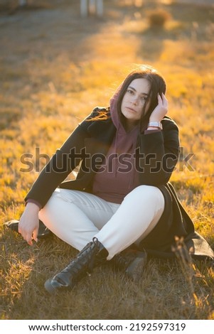 An attractive girl is sitting on the grass in the park and looking alone at the camera. Spending time alone Royalty-Free Stock Photo #2192597319