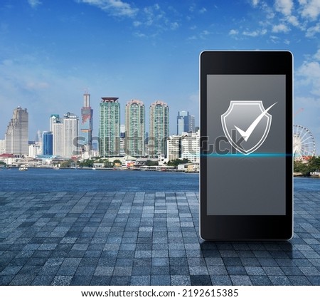 Security shield with check mark icon on modern smart mobile phone screen on stone tile floor over city tower, river and blue sky, Technology internet cyber security online concept
