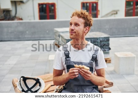 Taking a break. Young man working in uniform at construction at daytime.