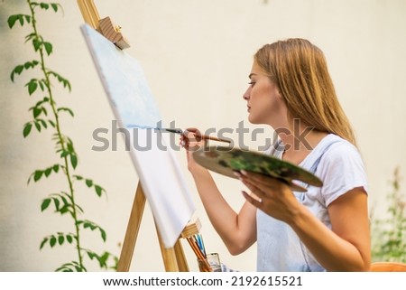 Woman enjoys painting on canvas outdoor.
