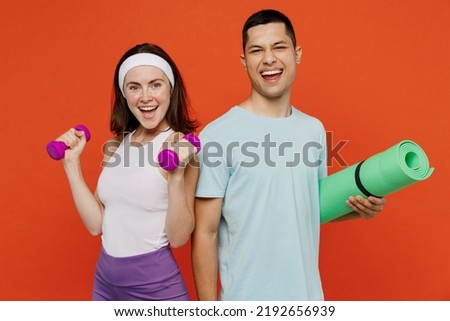 Young excited fitness trainer instructor sporty two man woman in headband t-shirt hold dumbbell yoga mat spend weekend in home gym isolated on plain orange background Workout sport lifestyle concept