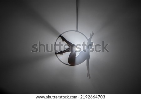 Aerial acrobat in the air ring. Young woman performs the acrobatic elements in the air hoop. Aerialist in on black background dark studio with backlight. For sports, acrobatic, circus school. Royalty-Free Stock Photo #2192664703