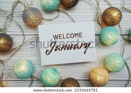Welcome January text on paper card with LED cotton balls top view on wooden background