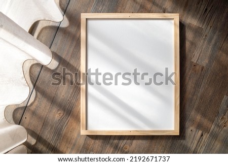 Blank white mockup template of a vertical 40x50cm poster canvas or picture with a pinewood frame. Background texture of elegant wall art display placed on wooden floor with curtain shadow overlay.