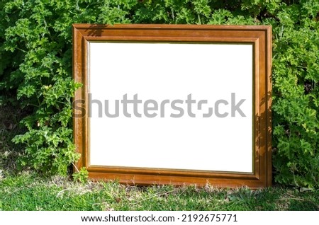 Blank white mockup wall art template with a weathered wooden frame placed outdoor in a garden. Background texture of painting or picture with natural sunlight surrounded by green leafy plants.