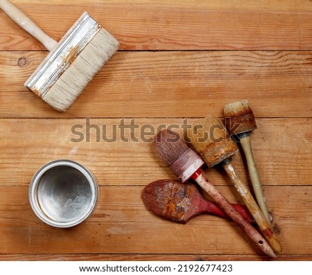 four old paint brushes and an empty metal can on wooden boards. View from above.
