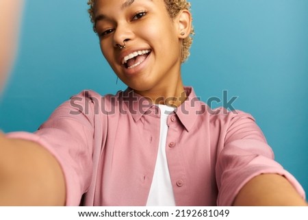 Closeup crop shot of happy smiling african american woman woman of 20s with blond curly short haircut making content for her social media profile, recording stories, taking selfie on front camera