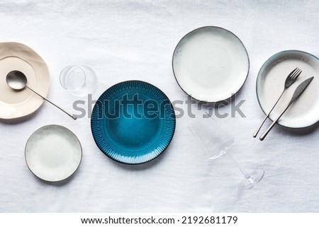 Modern tableware set with cutlery, glasses, and a vibrant blue plate, overhead flat lay shot. Trendy dinnerware on a tablecloth with copy space Royalty-Free Stock Photo #2192681179