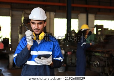 Technician engineer man in protective suit stand and use walkie talkie radio and tablet while controll or maintenance operation work lathe metal machine at heavy industry manufacturing factory Royalty-Free Stock Photo #2192688029