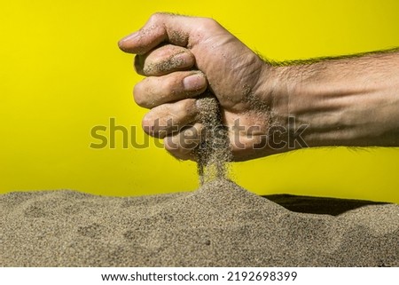 Sand pours through fingers on a yellow background. The concept of quickly passing time.