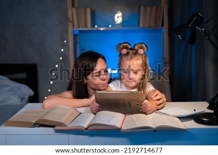 mom helps child daughter do homework at home using digital tablet. Child studying late at night. Children, family, education concept