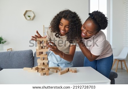 Family plays board game. Cheerful and friendly young woman and her teenage daughter are having fun playing Jenga together. Dark-skinned family spending time together at home on day off. Royalty-Free Stock Photo #2192728703