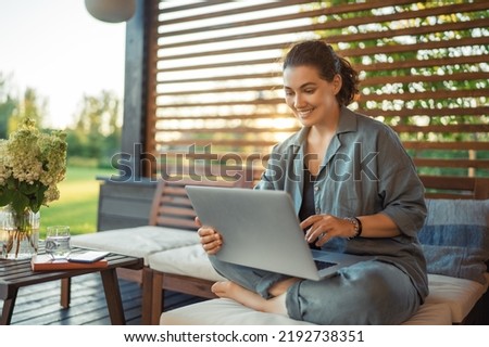 Happy young woman is working sitting on the patio in summer.