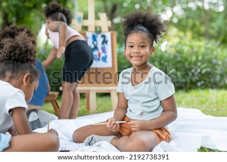 African American little girls with curly hair paint painting watercolor in summer park. Kid artist painter draw pictures outside.Education learning outdoor concept